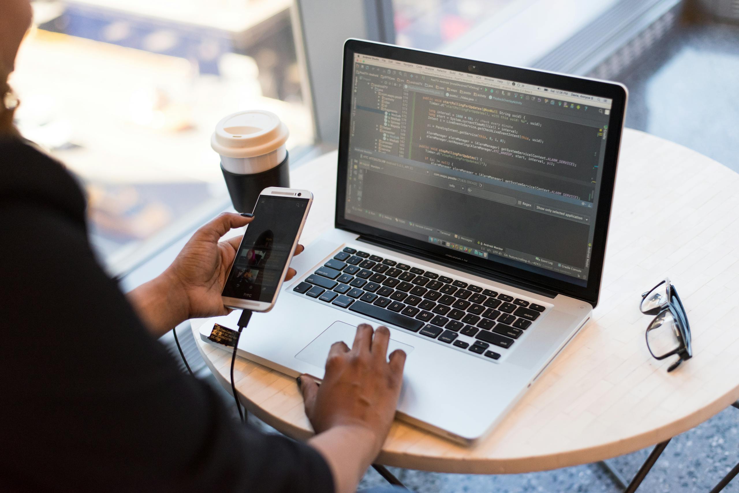 Developer working remotely, coding on a laptop with phone in hand, showcasing modern work culture. Ankara web tasarım, seo, reklam ajansı